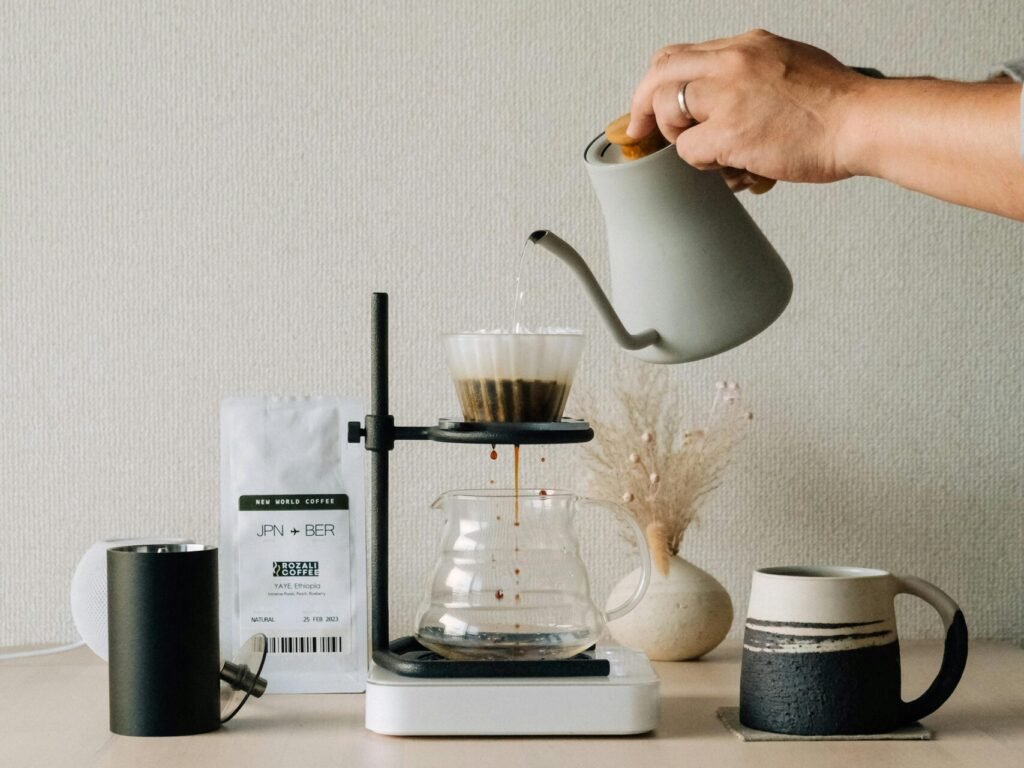 A hand pours water into a coffee filter using a kettle for pour-over brewing setup.